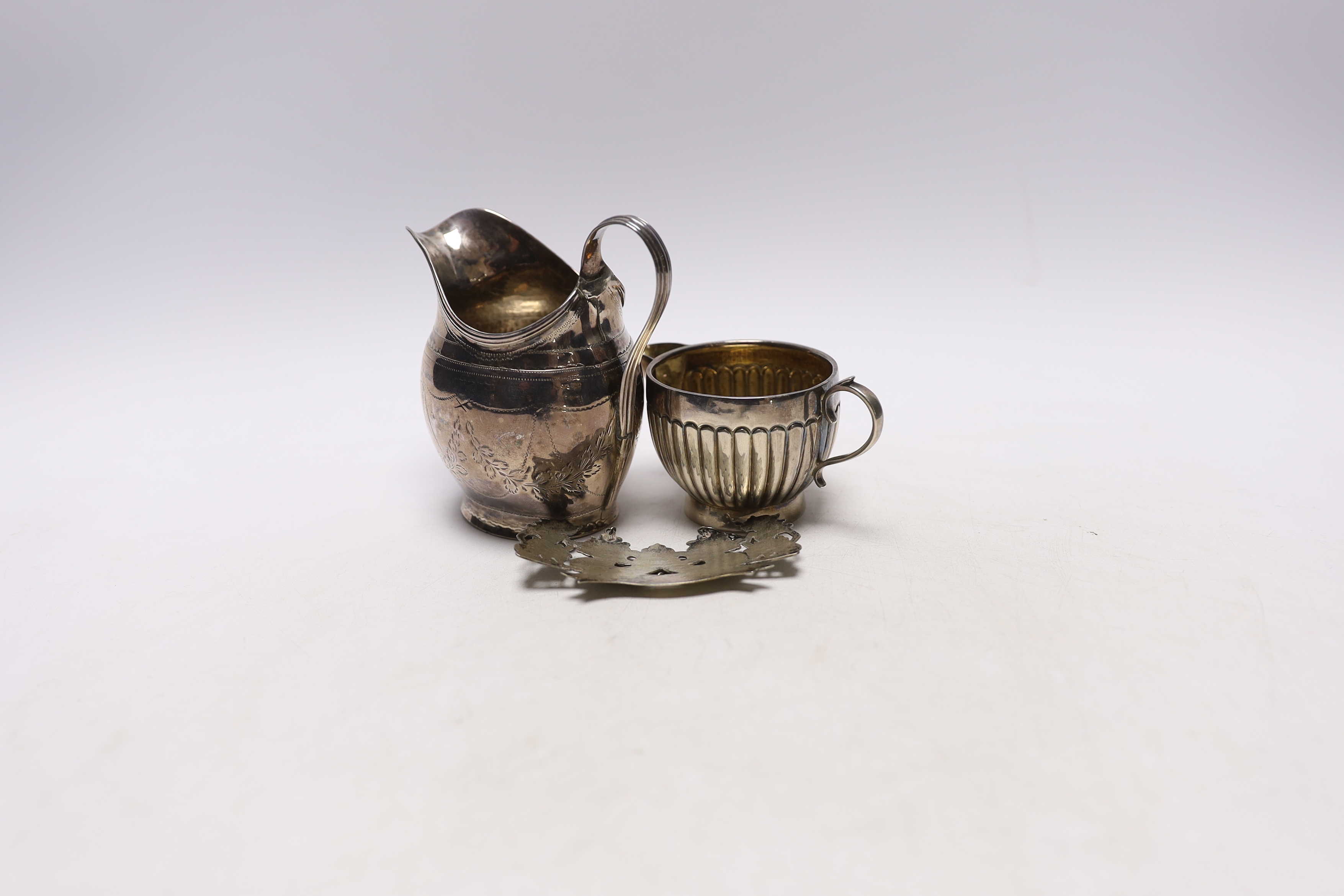 A George III silver helmet shaped cream jug, London, 1799 (a.f.), a Victorian silver cream jug by George Unite and a white metal whisky wine label.